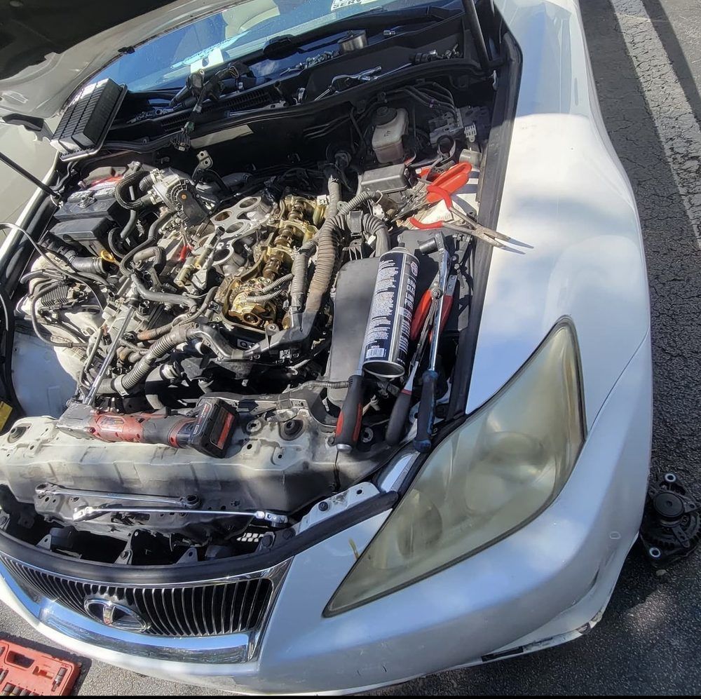 White car with the hood open, revealing the engine being worked on with tools scattered around.