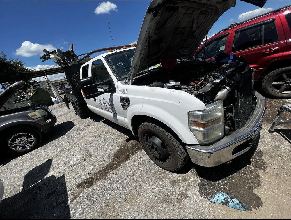 White pickup truck with hood open in a salvage yard, with a red SUV nearby.