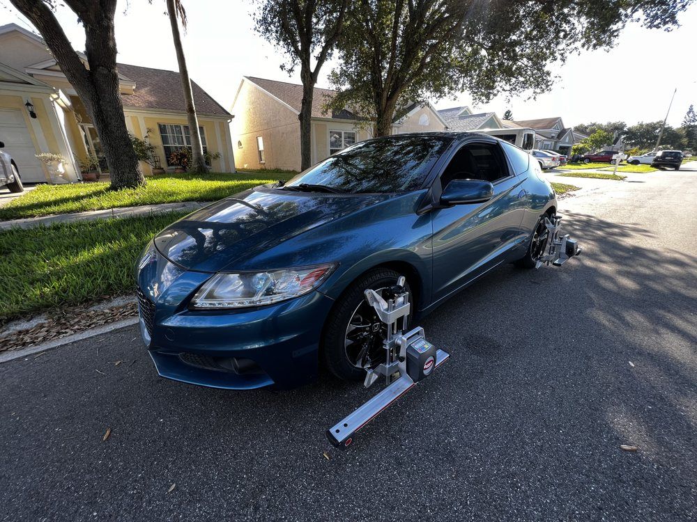 Blue car being aligned on a residential street; alignment equipment attached to front tire.