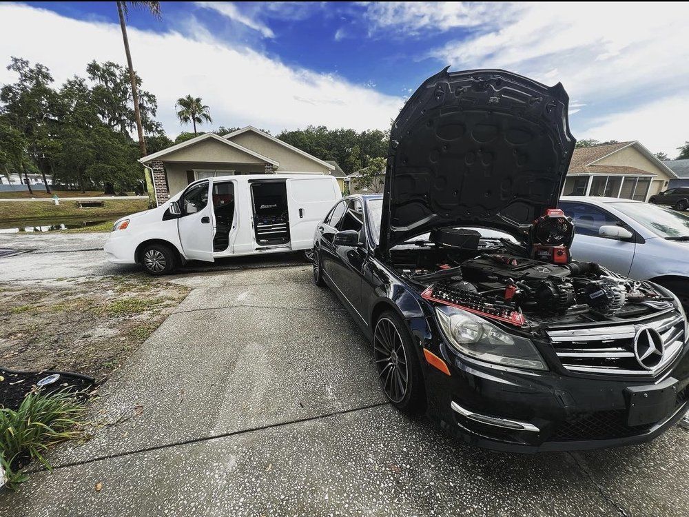 Black Mercedes with hood open, parked in front of a white van. Outdoor residential setting.