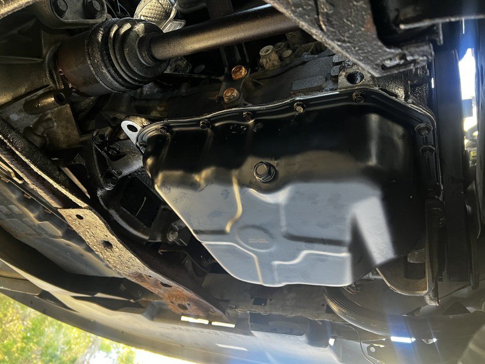 Underside view of a black oil pan on a car. Other car components are visible.