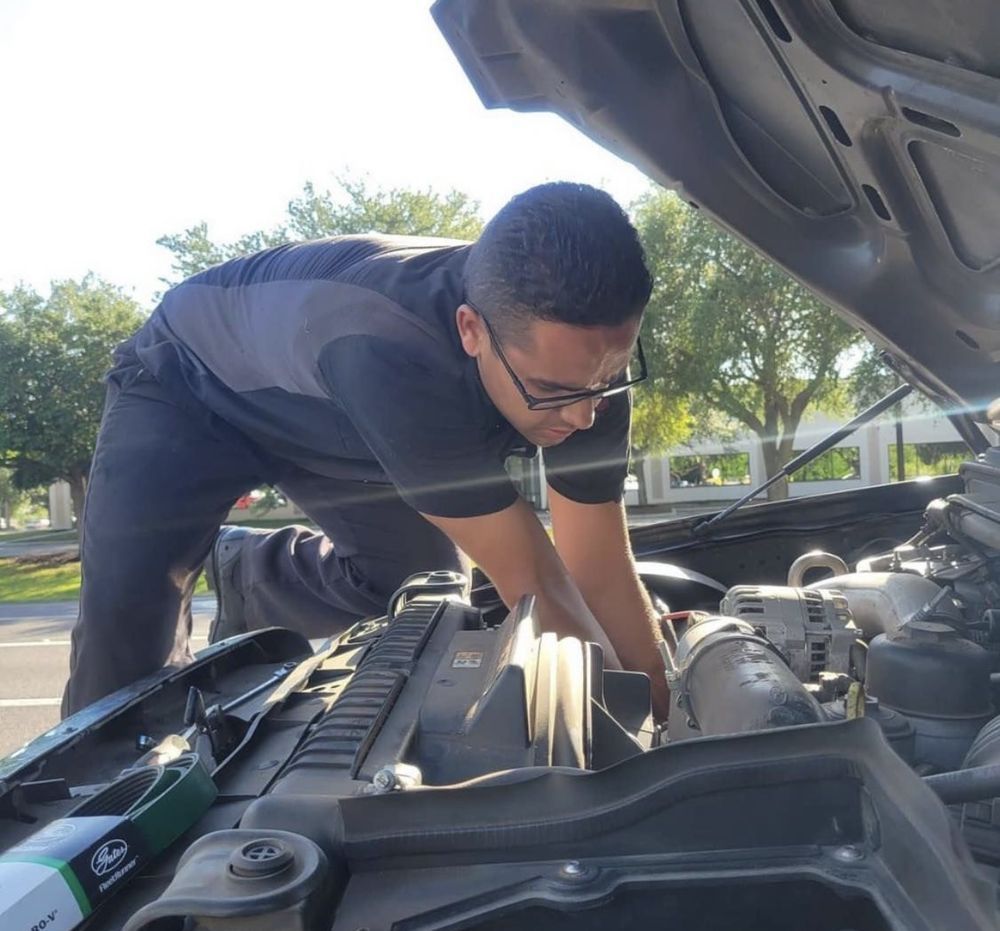Mechanic works on a car engine under the hood outdoors.