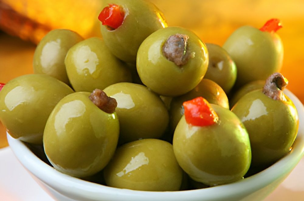 A Bowl of Green Olives With a Red Pepper on Top — Corrado & Frank Distributors in Fairy Meadow, NSW