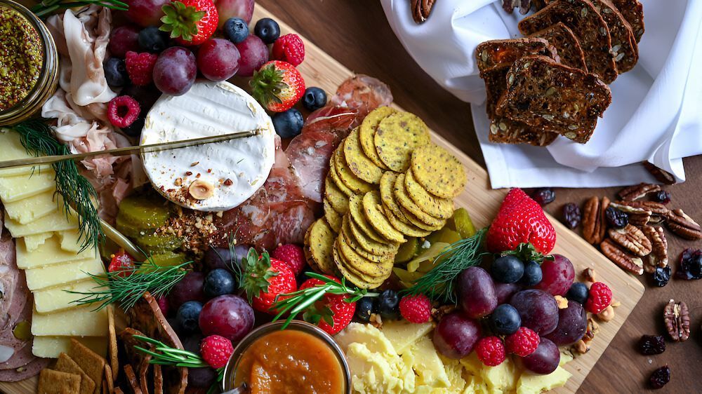 A Wooden Cutting Board Topped With Cheese , Crackers , Fruit and Bread — Corrado & Frank Distributors in Fairy Meadow, NSW