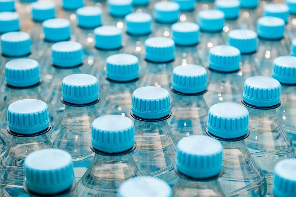 A Bunch of Plastic Water Bottles With Blue Caps on a Table — Corrado & Frank Distributors in Fairy Meadow, NSW