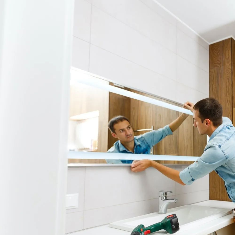 A man hangs a lighted mirror on a bathroom wall