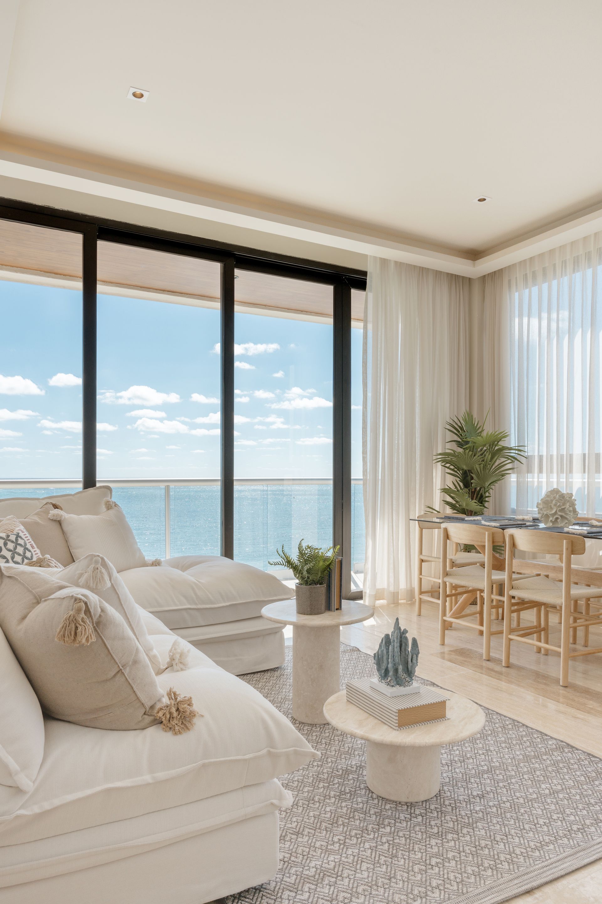 A living room with a couch , table , chairs and a view of the ocean.
