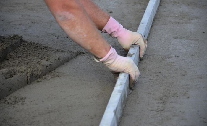 Maple Ridge Concrete worker repairing a concrete driveway by placing new concrete and screeding with a metal tool.