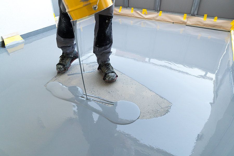 Maple Ridge Concrete employee pouring concrete sealer onto a concrete slab. The worker is wearing black jeans.