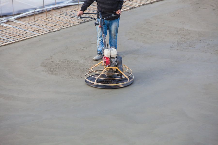 Concrete in maple Ridge being polished by a worker wearing blue jeans and a black sweater. The man is operating a steel powered trowel.