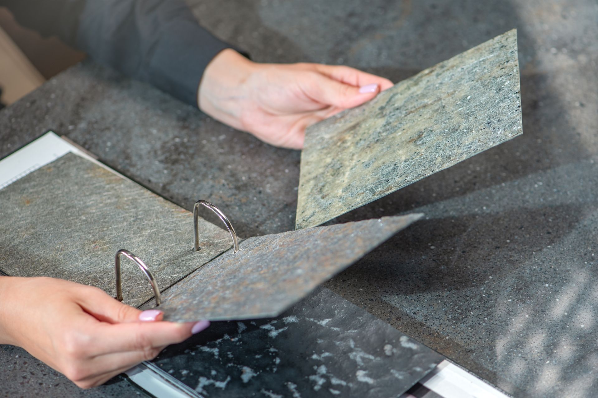 Hands holding and comparing stone countertop samples of various colors.