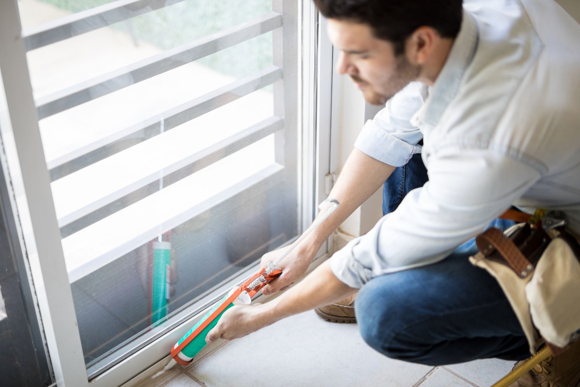 Man caulking around a sliding glass door frame; he is kneeling inside.