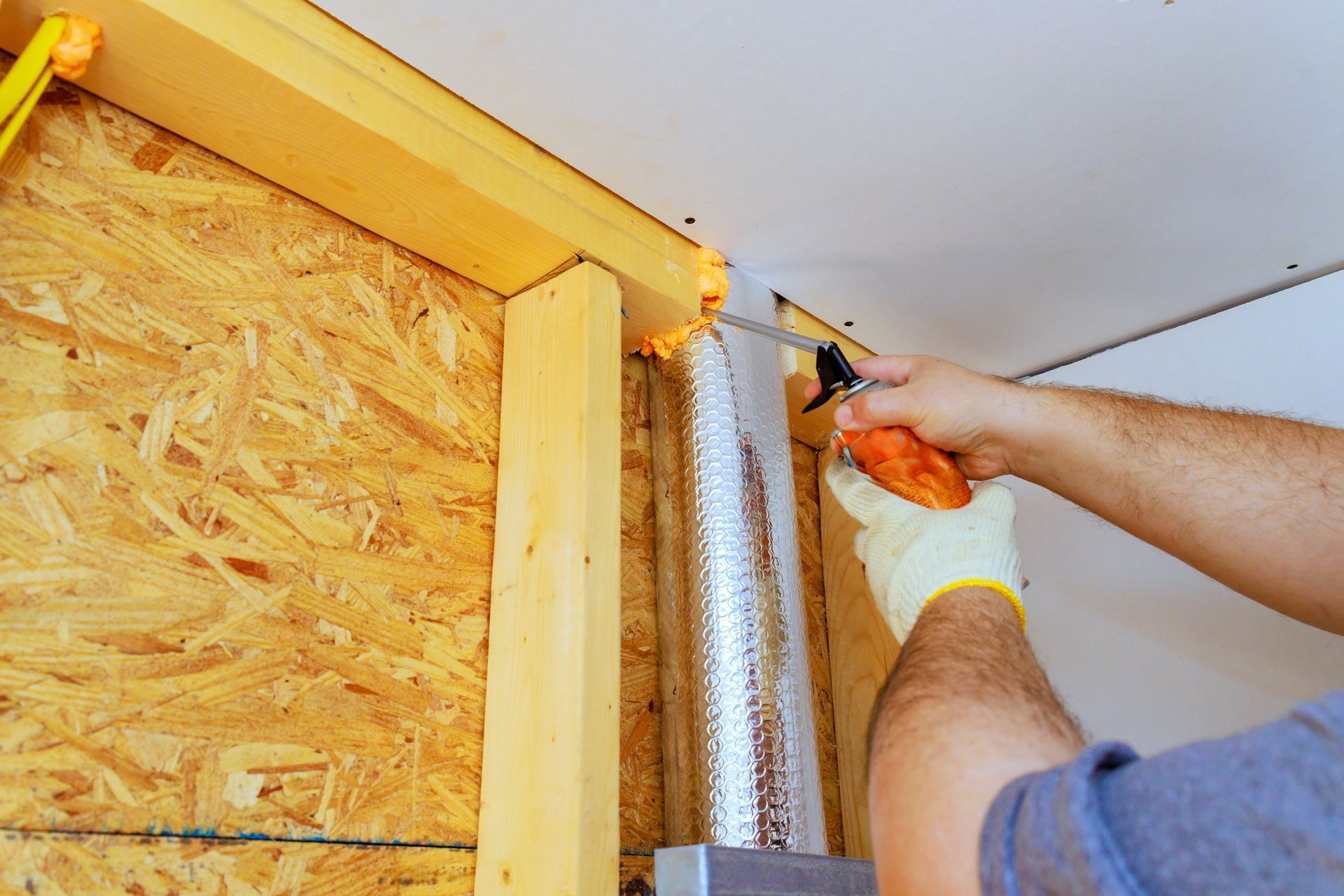 Person sealing a silver duct with orange foam from a caulk gun.
