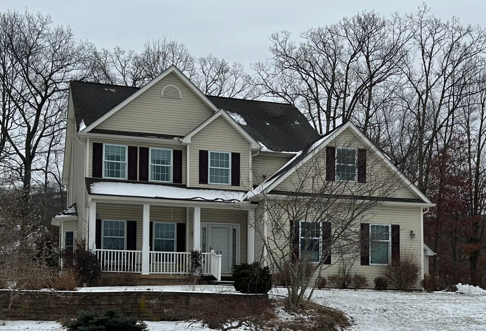 A large house with black shutters and a porch in the snow
