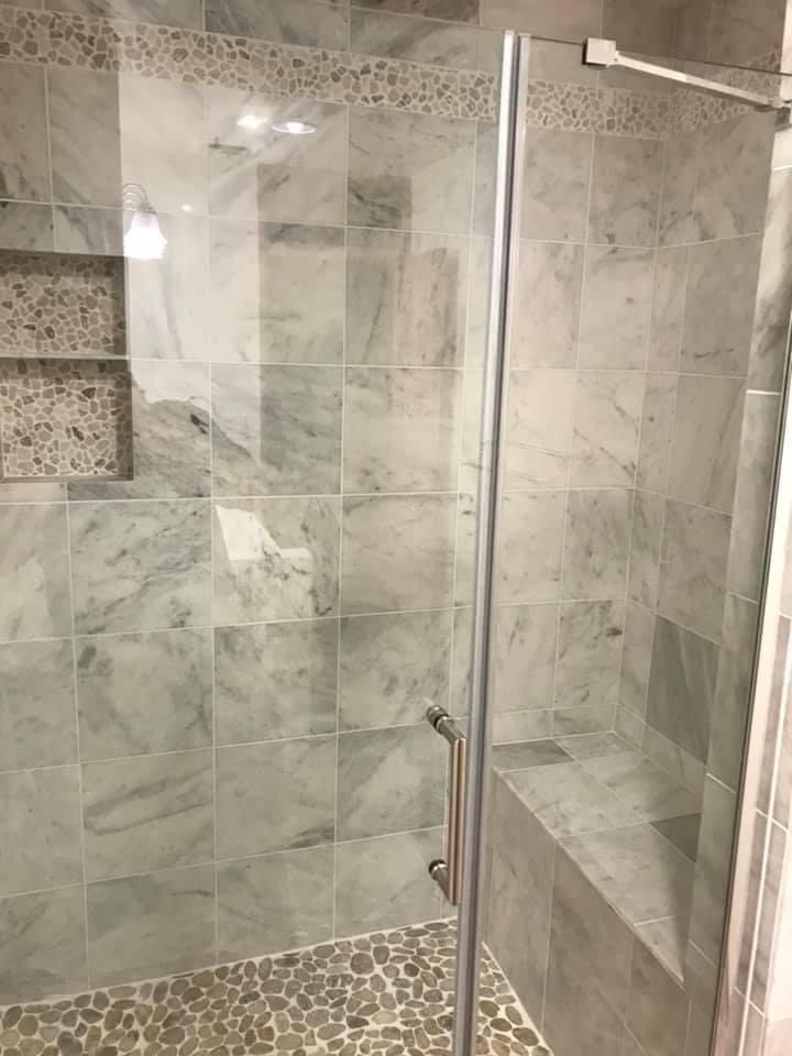 A walk in shower with marble tiles and a glass door.