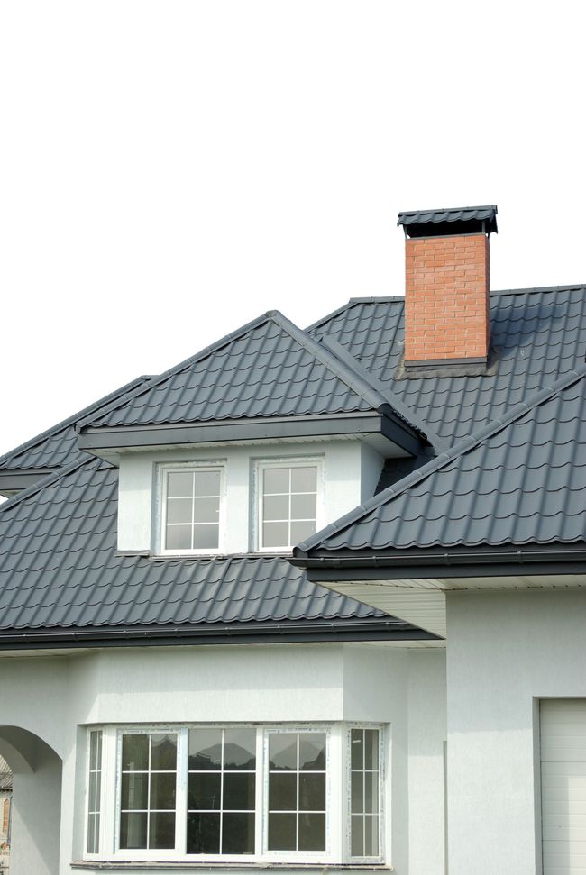 A white house with a black roof and a chimney on the roof.