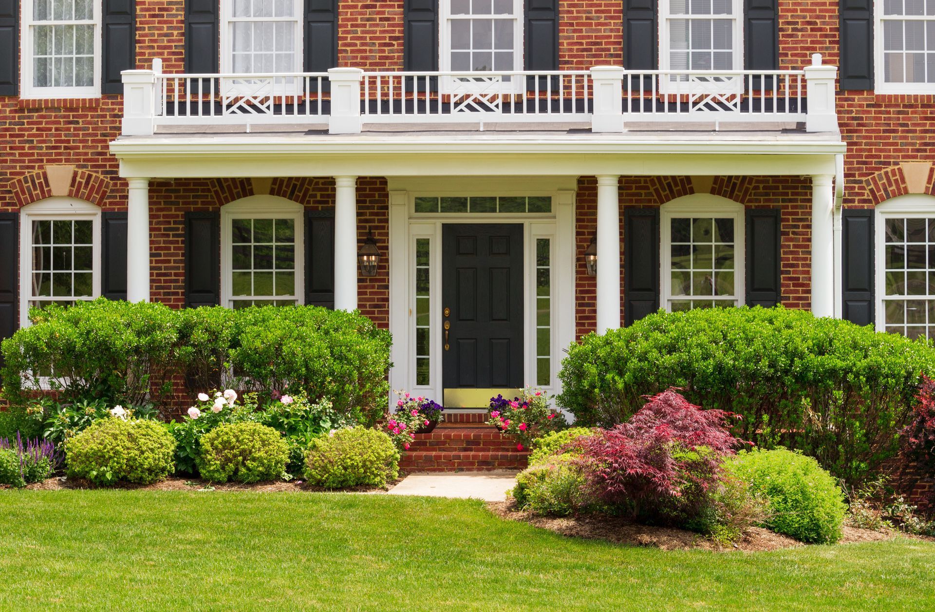 A large brick house with black shutters and a large porch