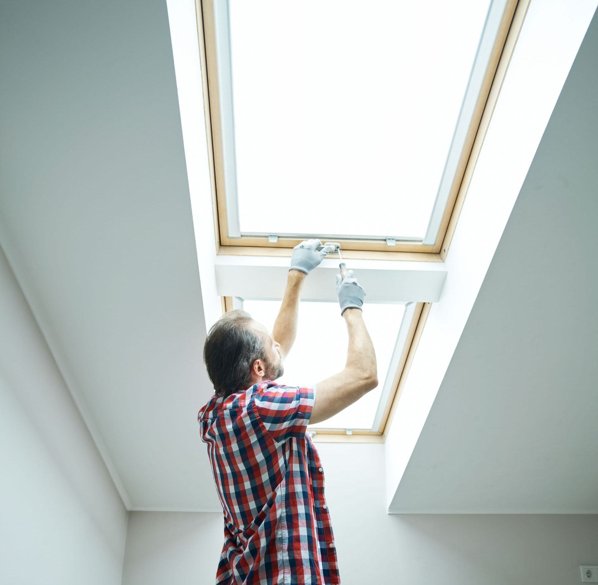 A man is working on a skylight in a room.
