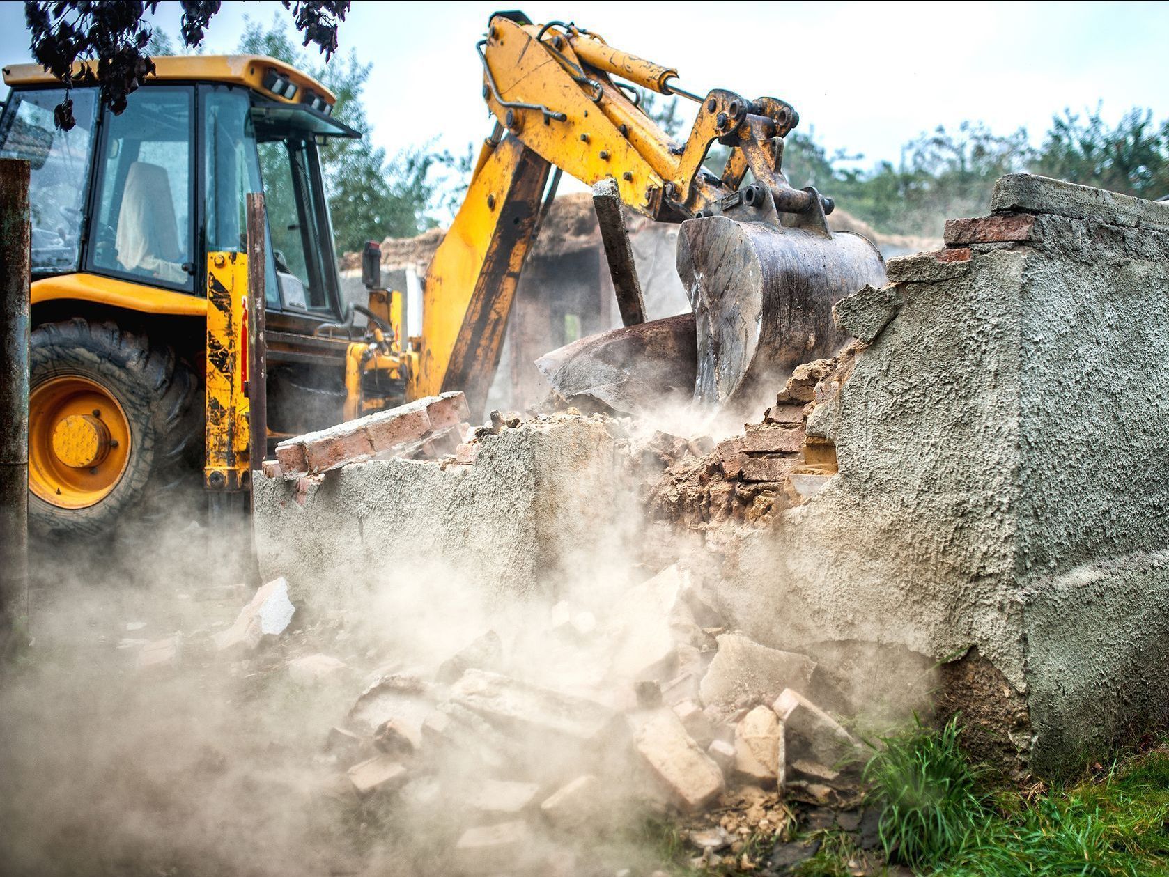 A yellow bulldozer is demolishing a stone wall.