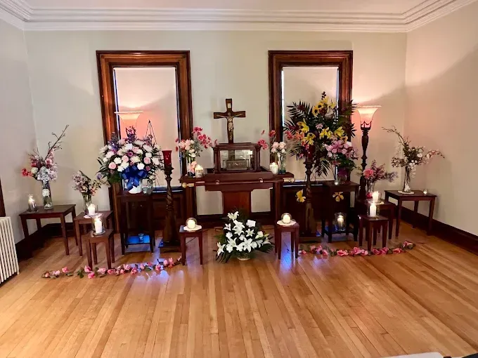 A man is standing in front of a coffin with flowers on it.