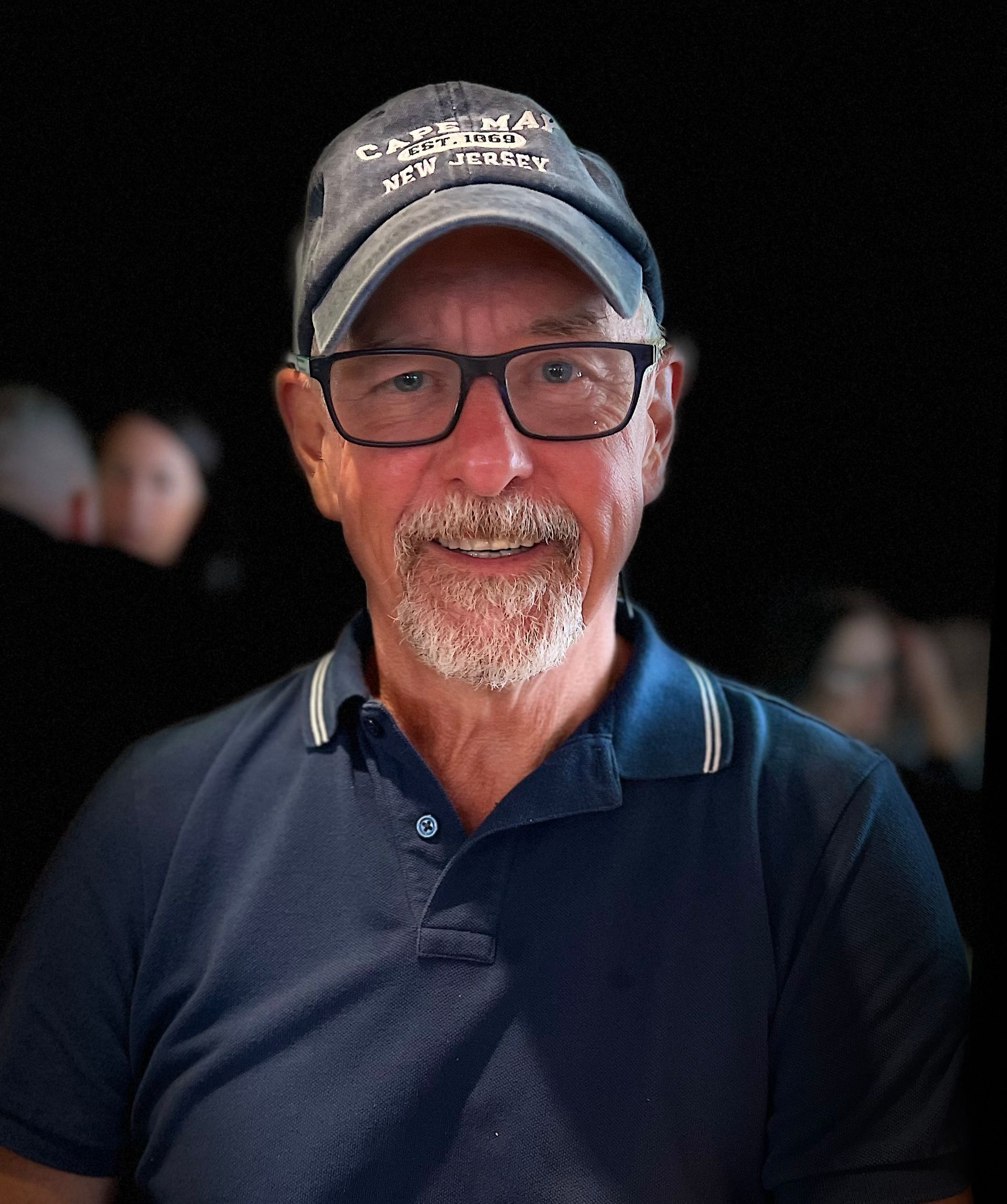 Man smiles between two children on carousel horses; outdoors, green trees visible.