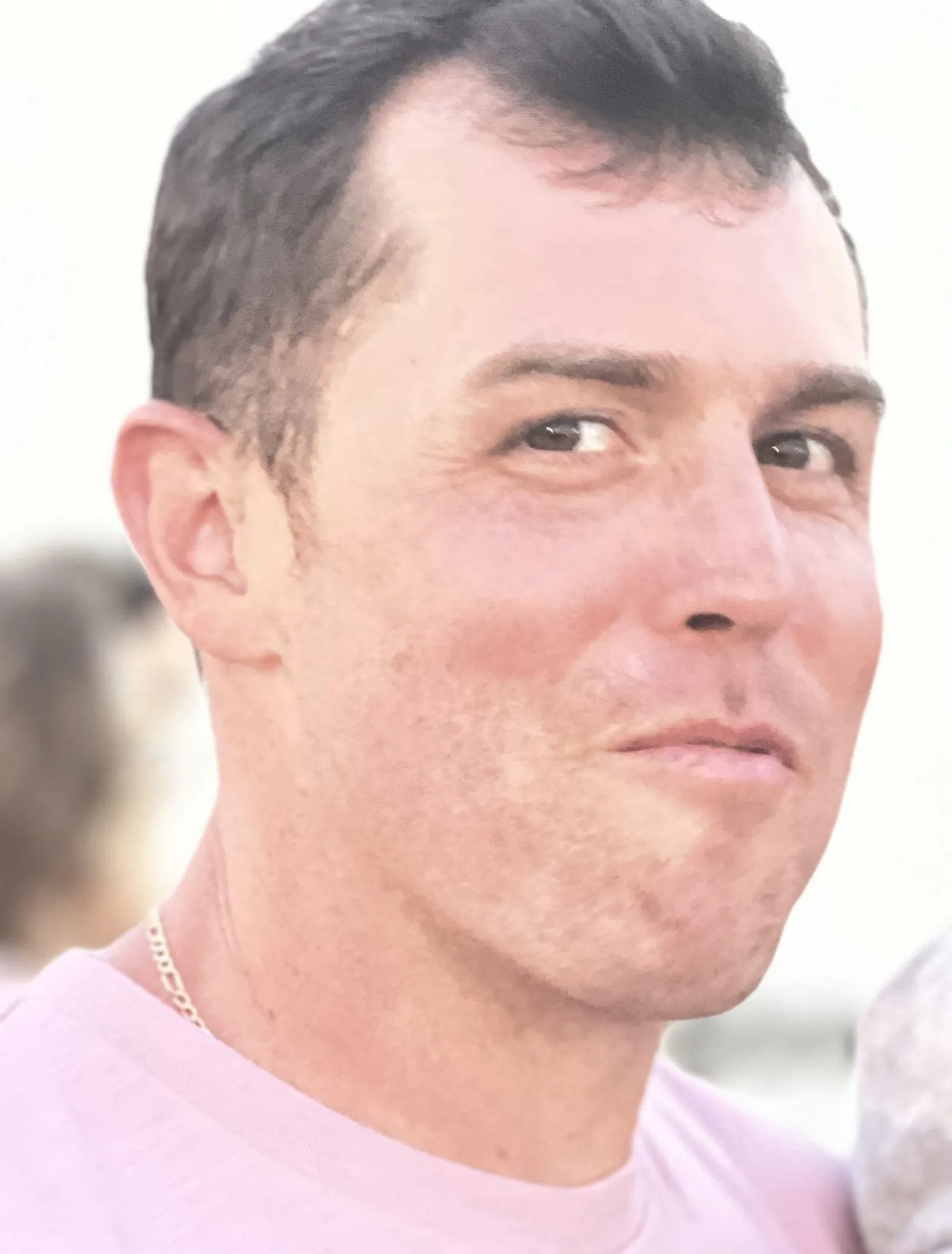 Man with short dark hair, wearing a pink shirt, looking at the camera with a slight smile.