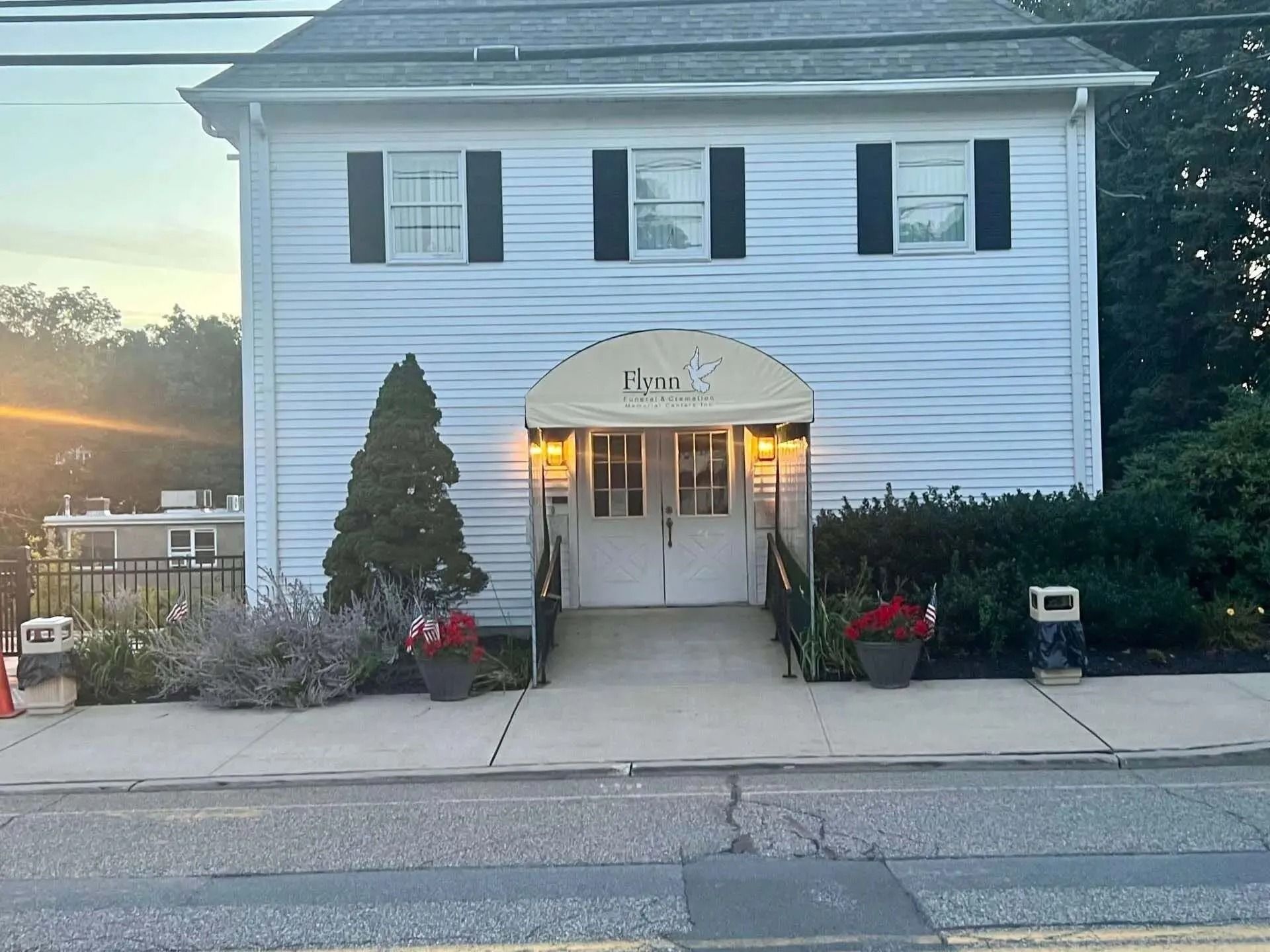 White building with awning over double doors; sidewalk, flower pots, and street visible.