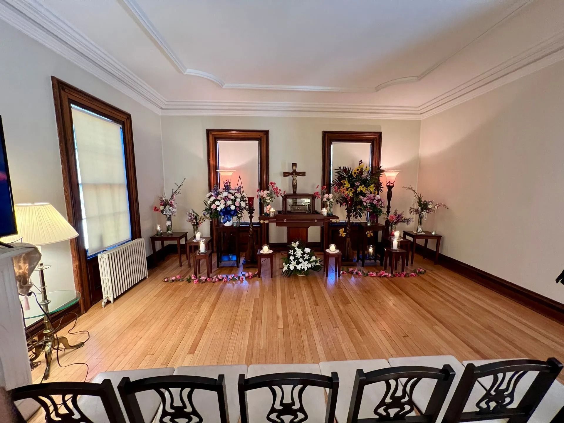 A funeral service setup in a room with flowers, candles, a cross, and chairs.