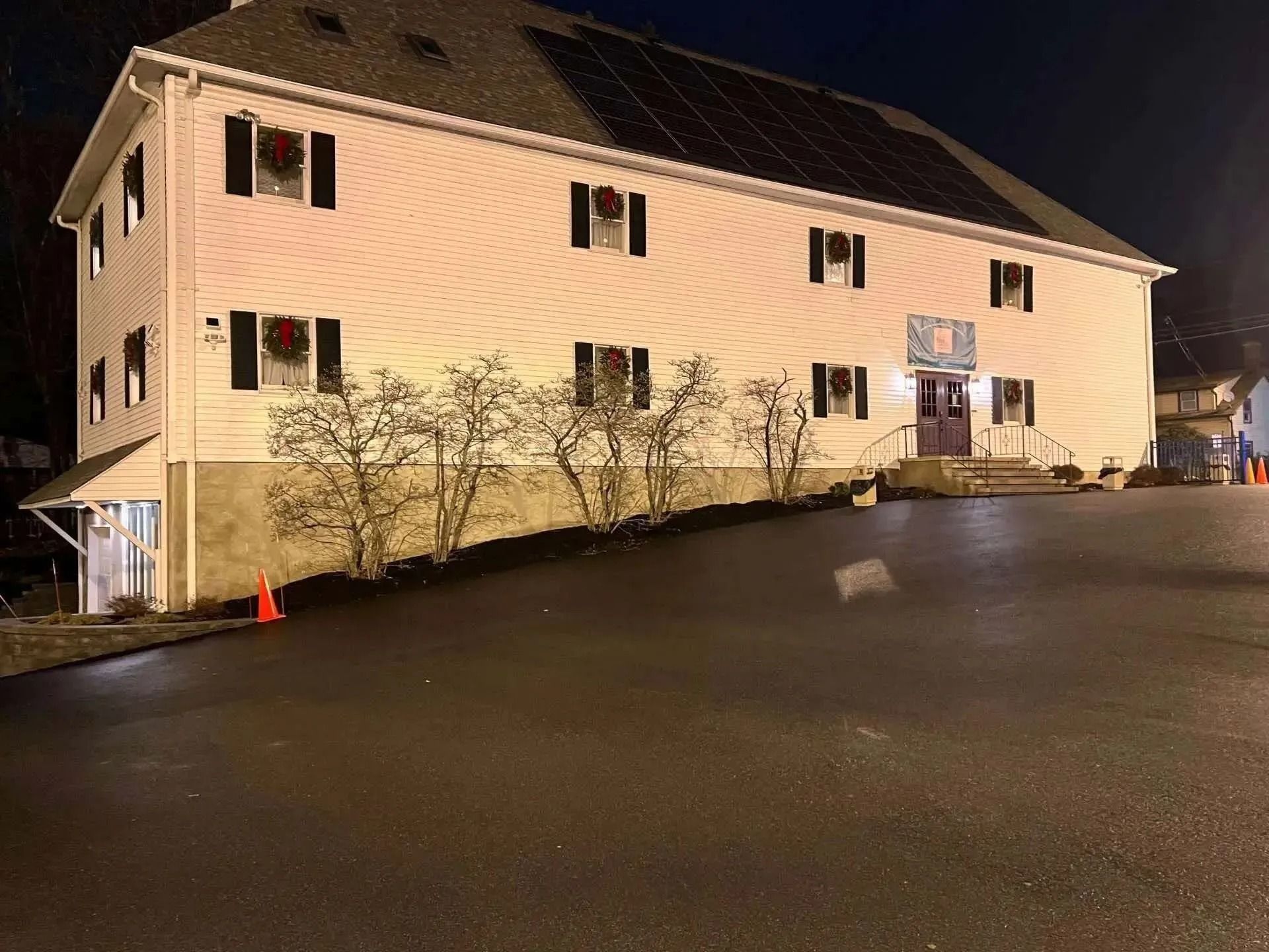 Three-story building with solar panels, black shutters, and Christmas wreaths. Asphalt driveway.