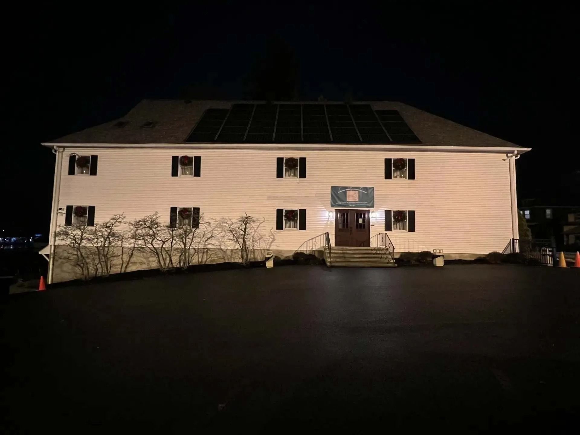 White two-story building at night with solar panels on the roof and a sign above the front door.