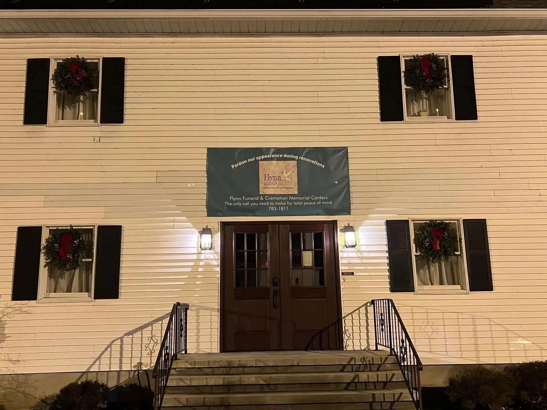 White building with double doors, shutters, wreaths, and a banner reading 