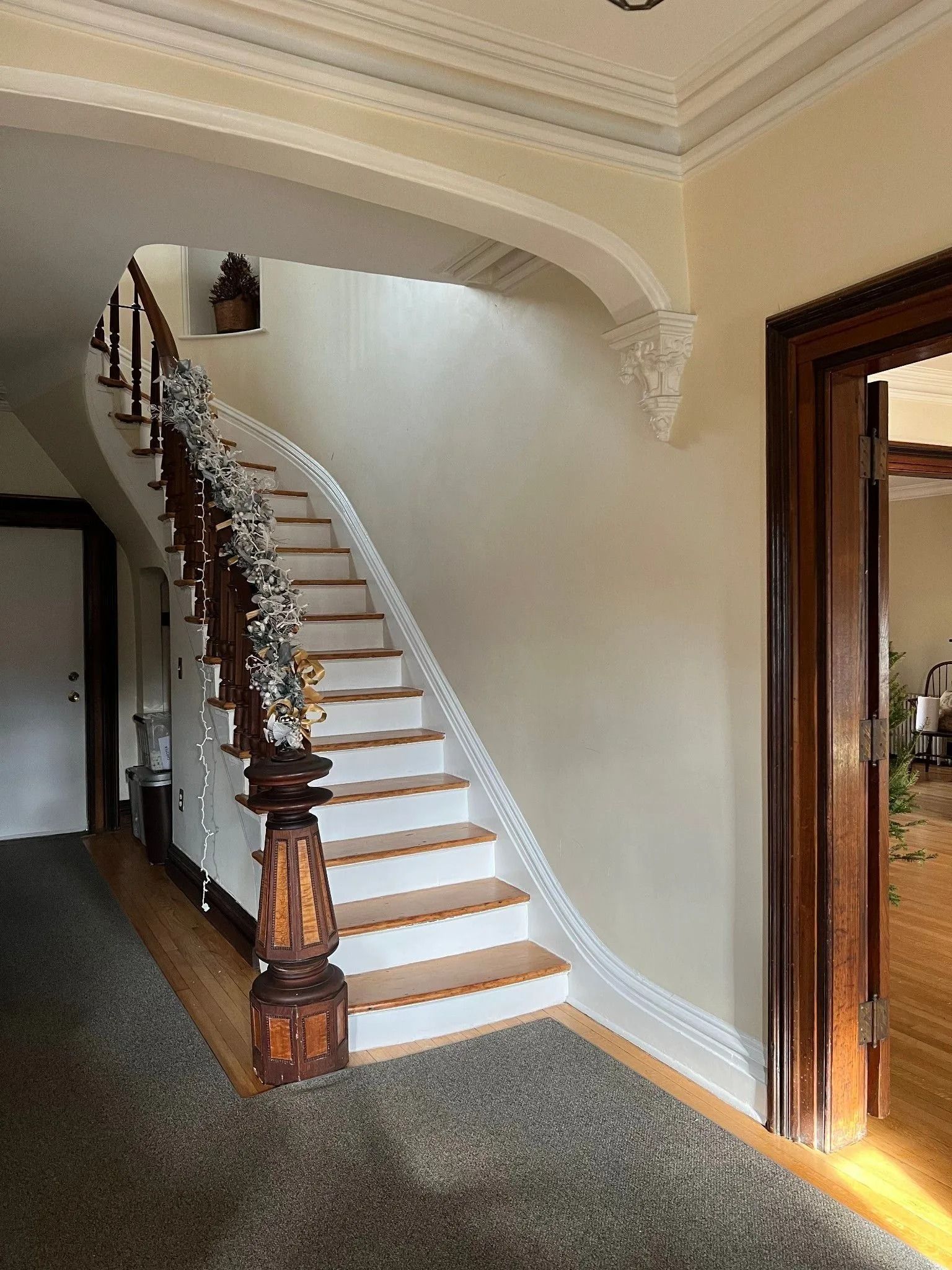 Staircase with ornate wooden banister and white risers against a cream-colored wall.