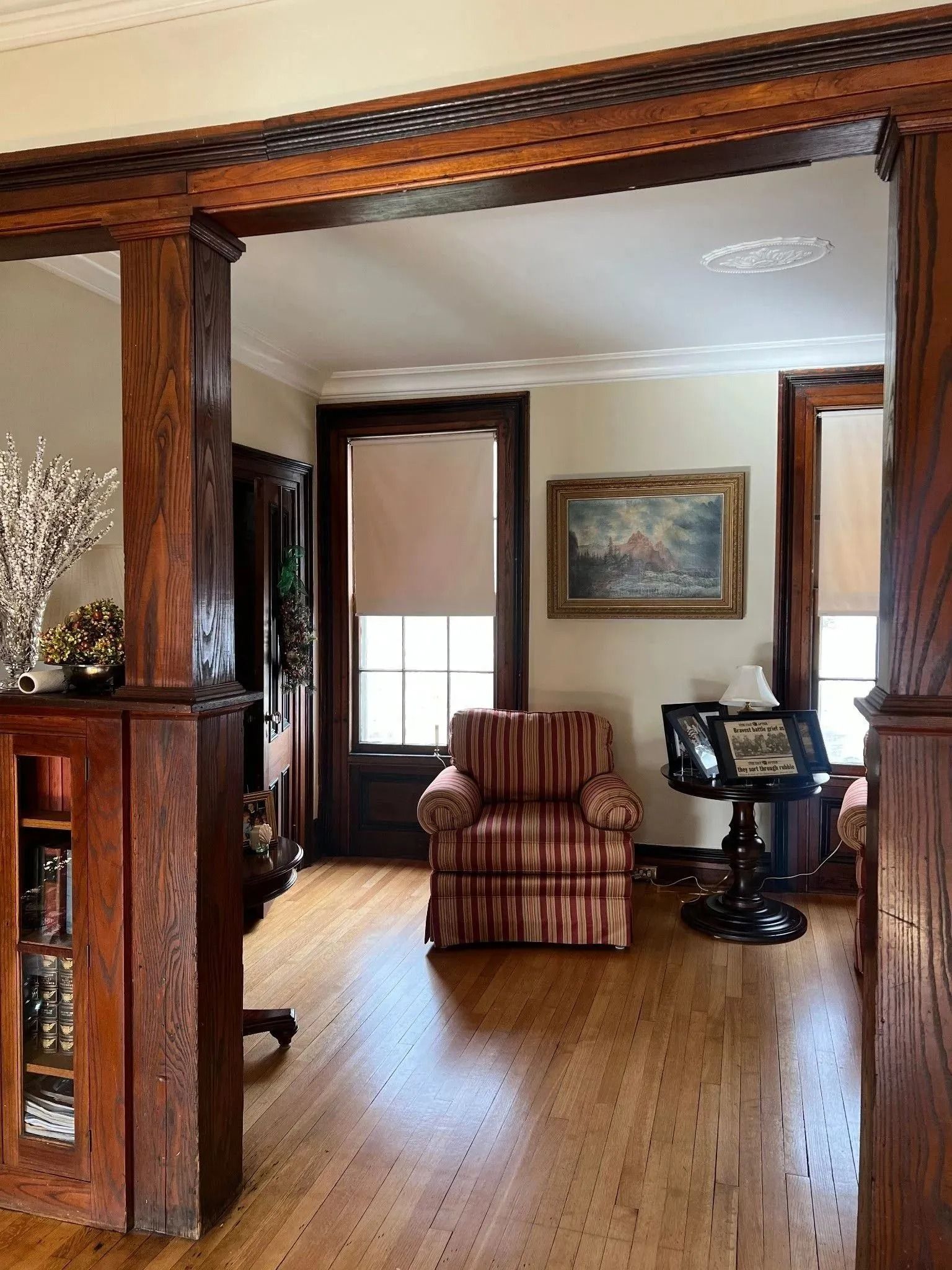 Wooden framed doorway opening to a room with an upholstered chair, painting, and round table; hardwood floor.
