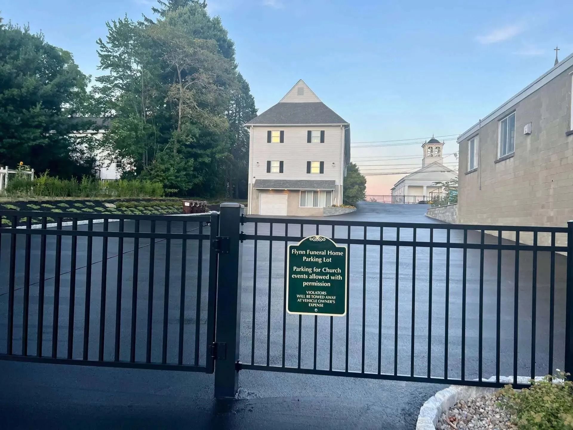Black gate in front of a light-colored building with a sign and a building in the background.