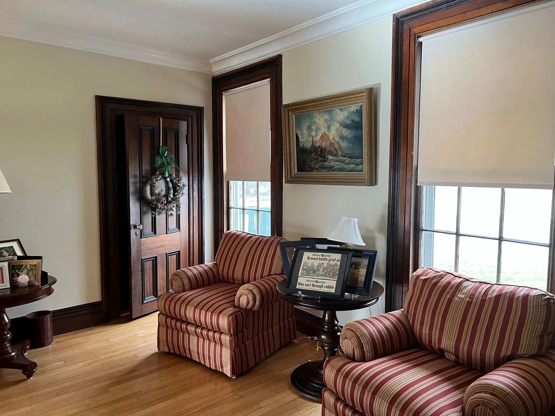 Cozy room with two striped armchairs, windows with blinds, dark wood trim, artwork, and a wreath on a door.