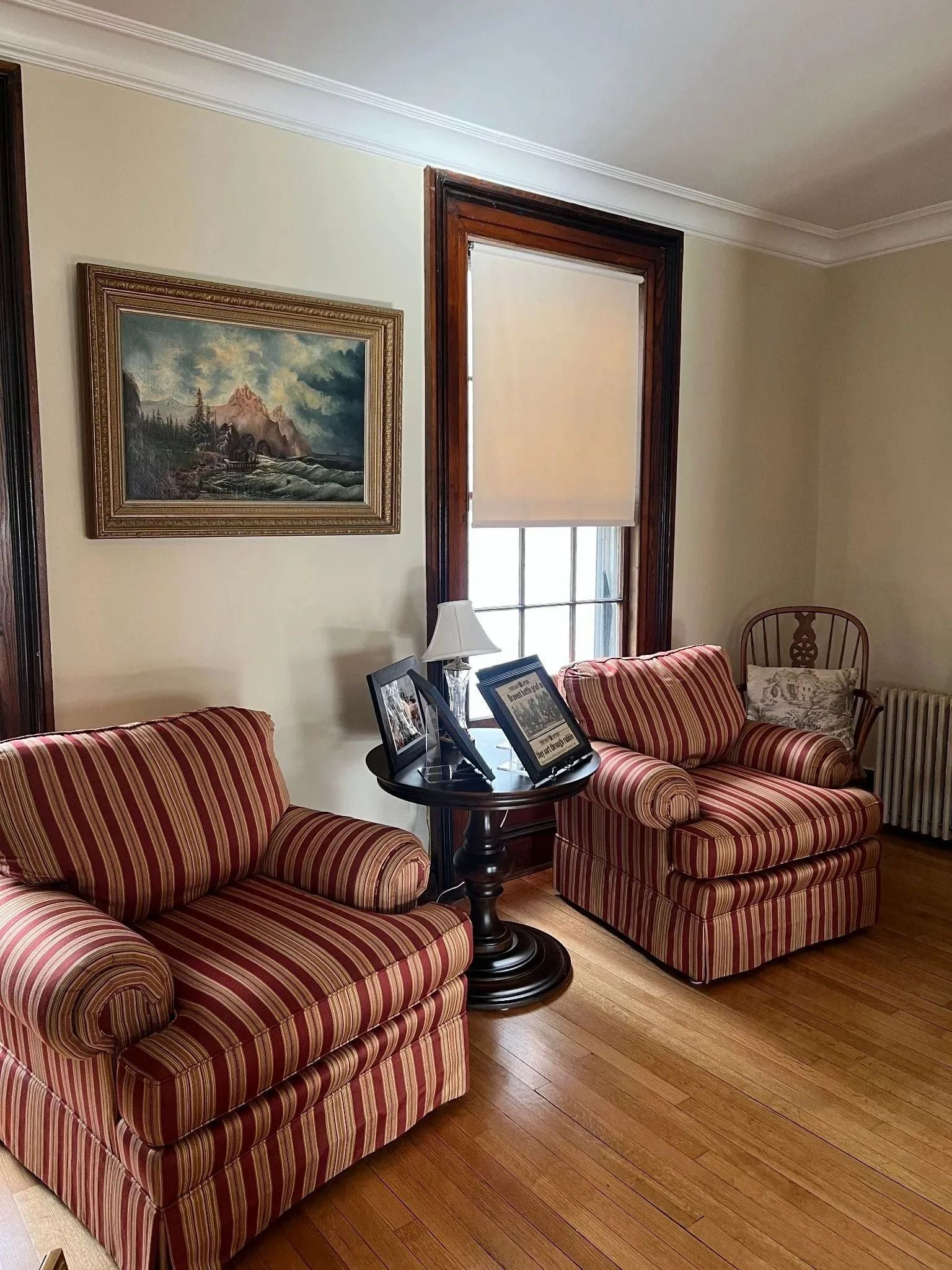 Two striped armchairs face a small table by a window, with a painting on the wall.