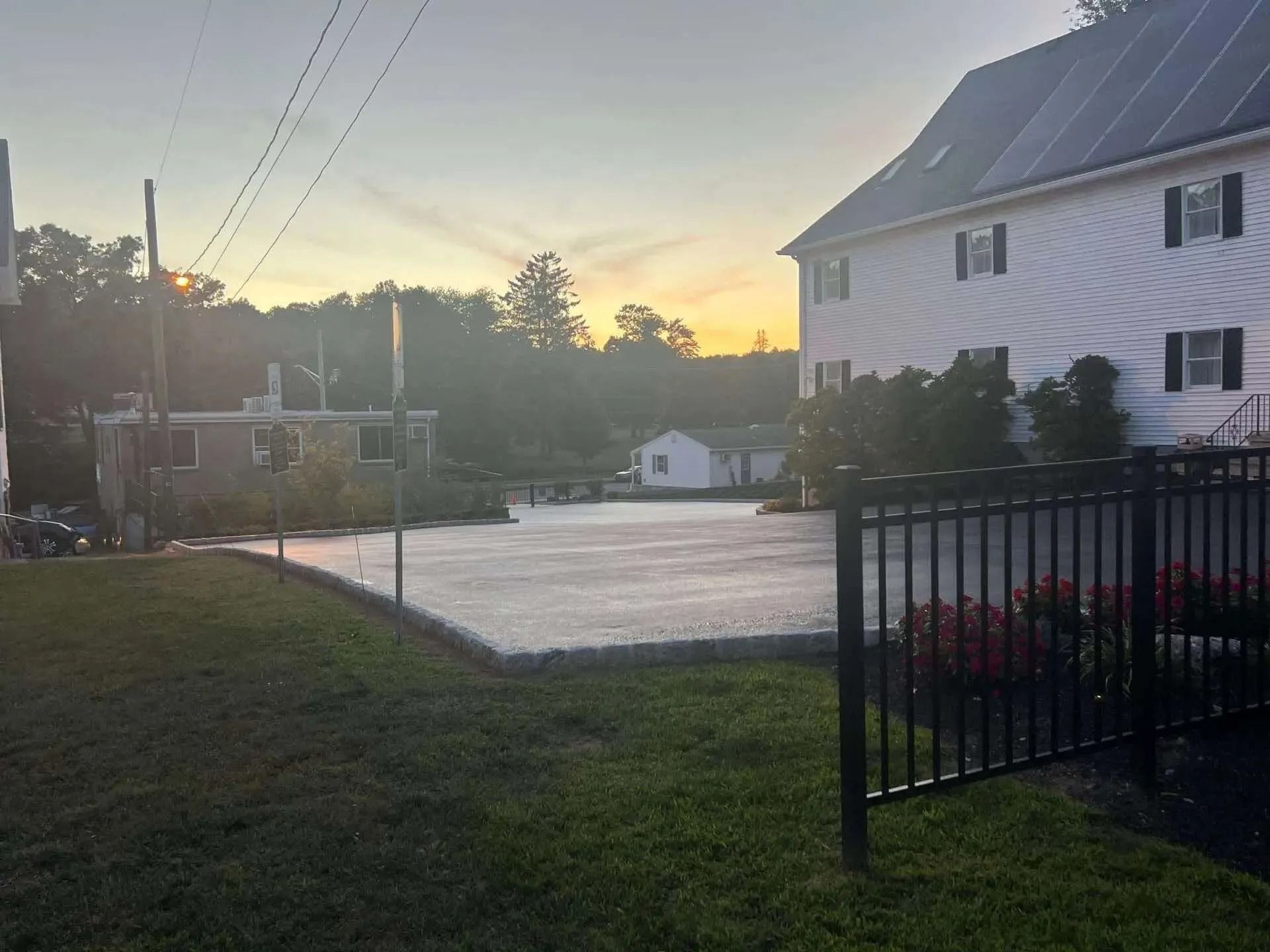 Sunset over a building with solar panels and a parking area, viewed from a grassy lawn.