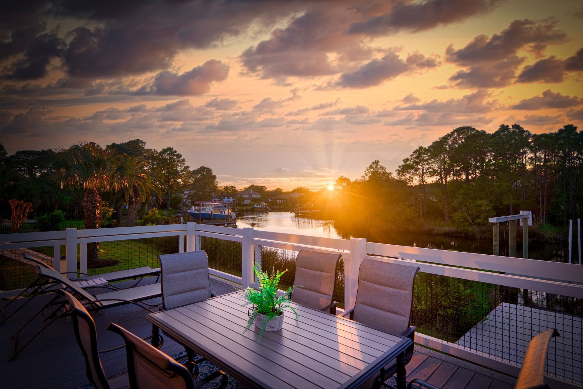 Sunset over a waterway viewed from a deck with a table and chairs.