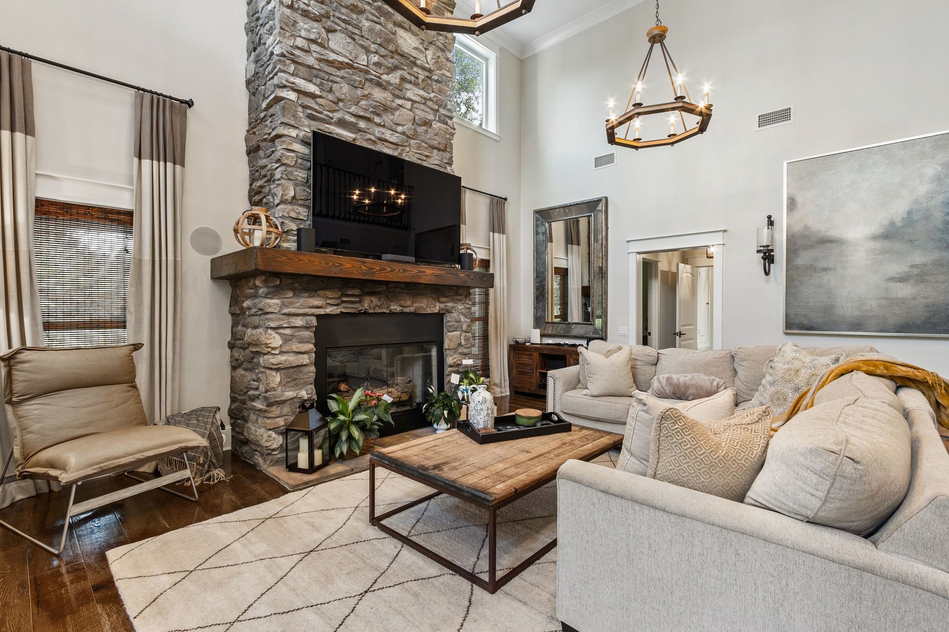 Living room with stone fireplace, sofas, rug, and chandeliers.