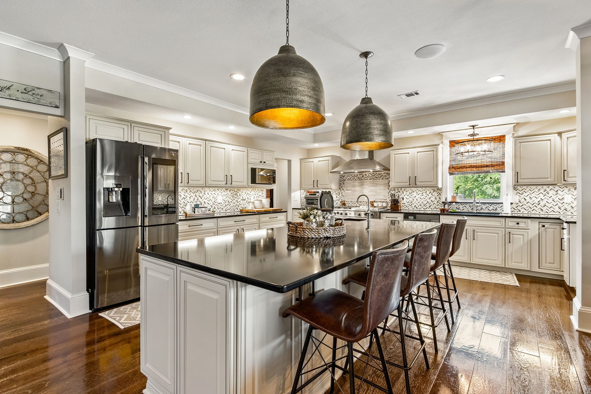 Modern kitchen with island, stainless steel appliances, dark counters, pendant lights, and wooden floor.