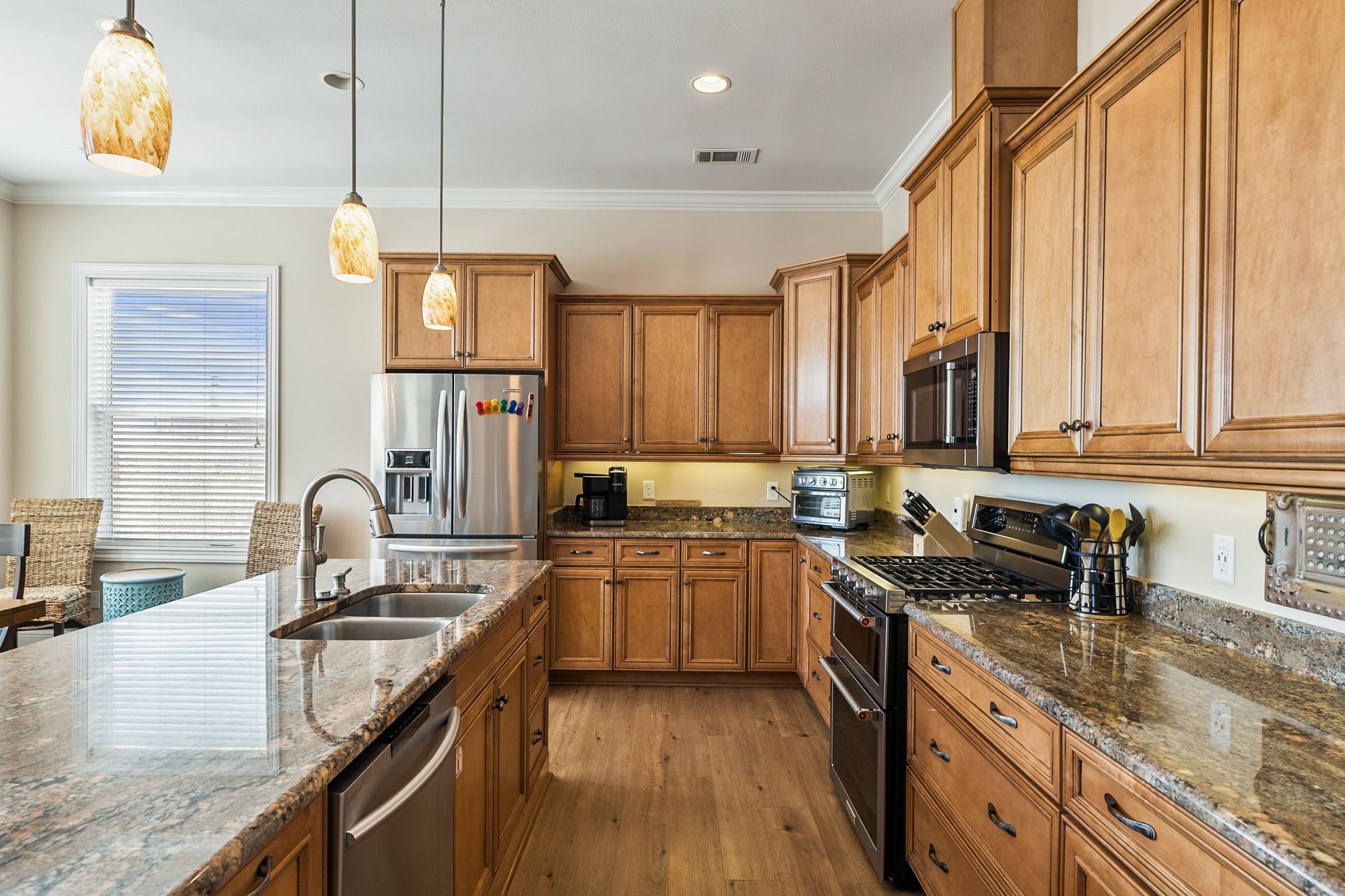 A kitchen with light wood cabinets, granite countertops, stainless steel appliances, and pendant lights.