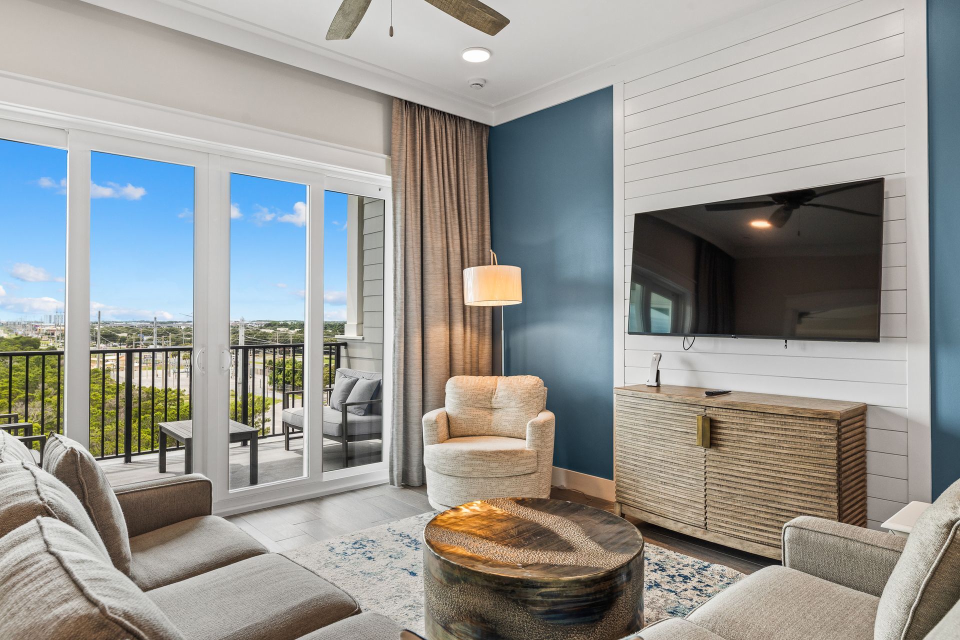 Living room with blue accent wall, large windows to a balcony, and beige furniture.
