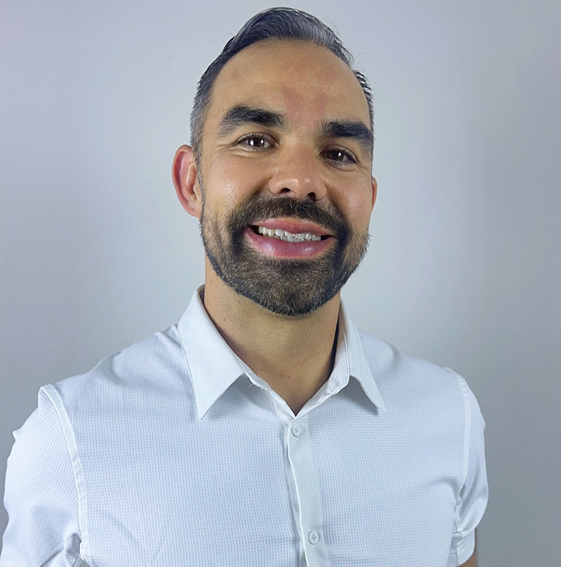 A man with a beard is wearing a white shirt and smiling.
