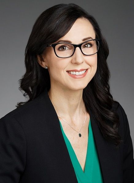 A woman wearing glasses and a green shirt is smiling for the camera.