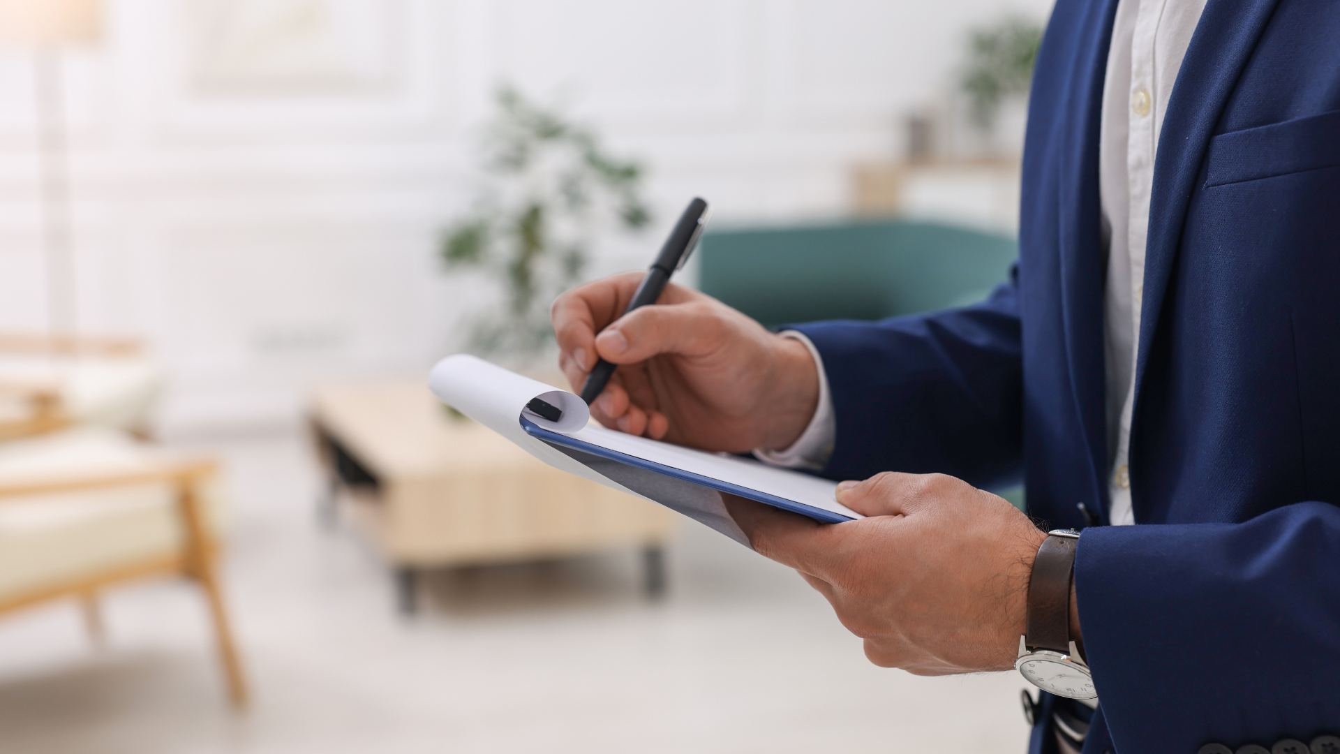 Person in blue suit writing on a notepad in a living room.