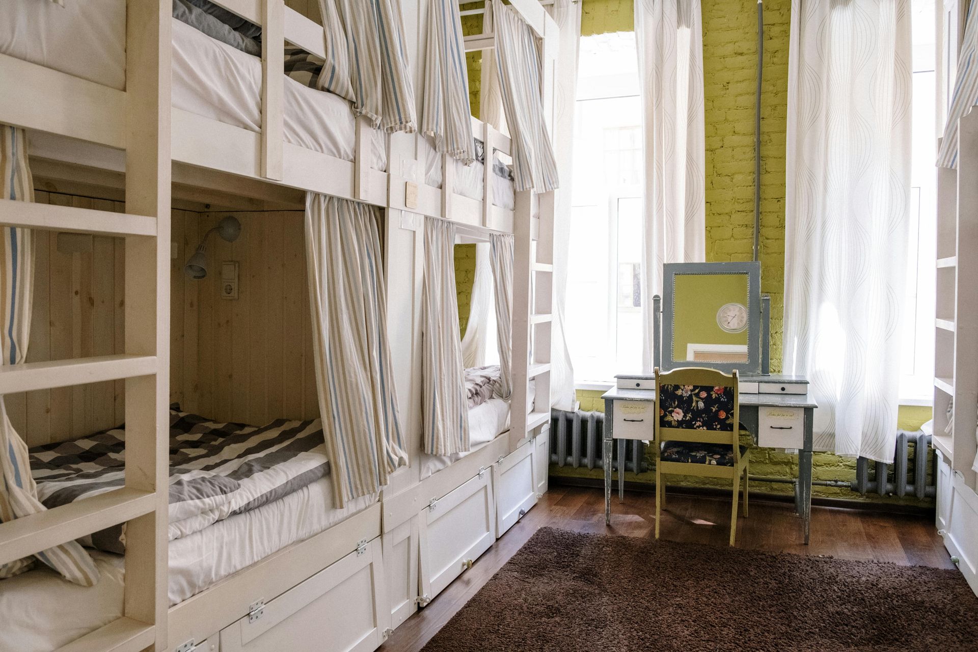 Bunk beds in a brightly lit room with white curtains, a dresser, and a brown rug.