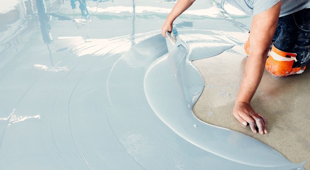 Person applying a light blue epoxy floor coating with a trowel.