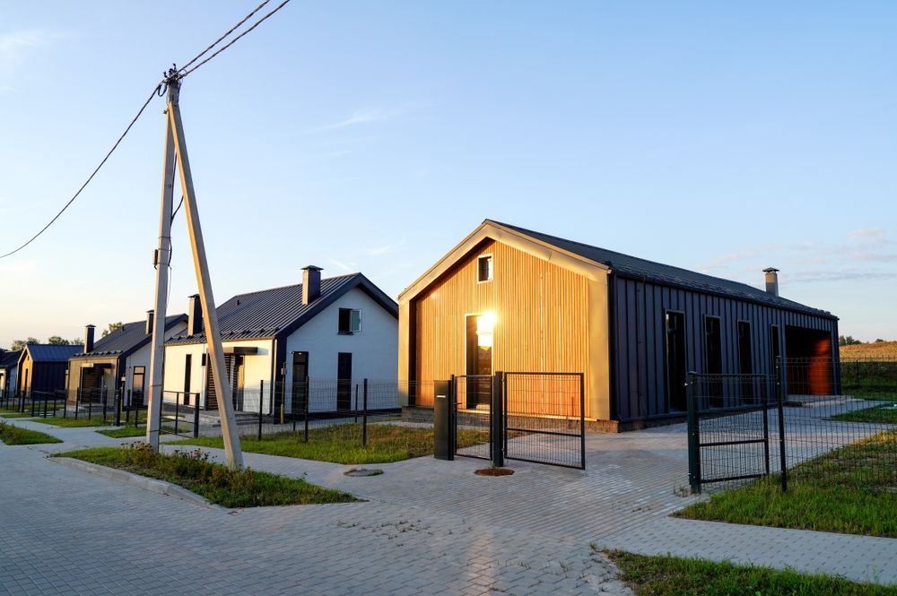 Modern wooden houses along a paved road. Open gate, utility pole.