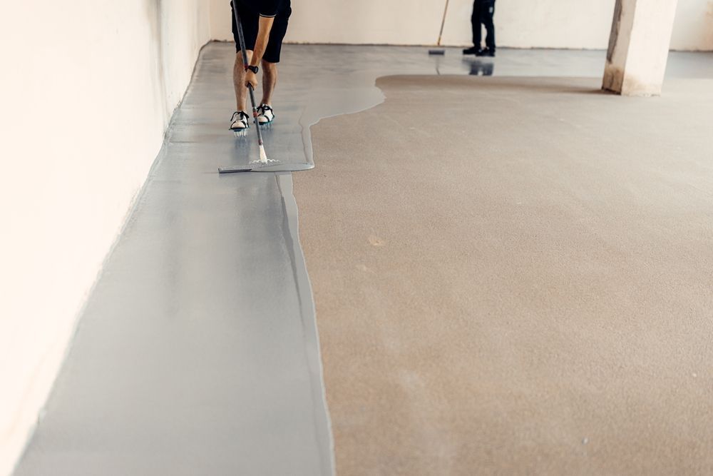 Two people applying gray epoxy to a concrete floor with tools in a construction setting.