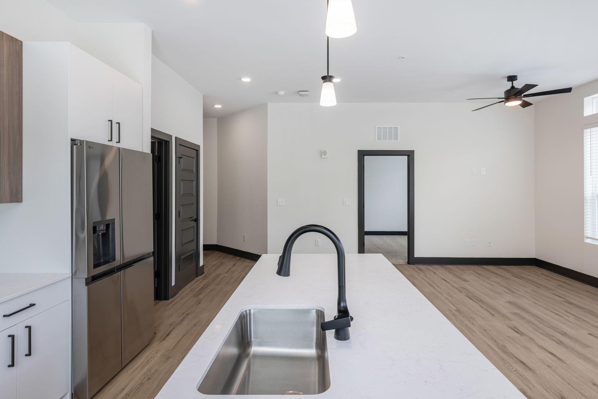 Modern empty kitchen with white cabinets, stainless appliances, island sink, and wood floors leading to an open room at Vela Park apartments in East Lake, Atlanta, GA.